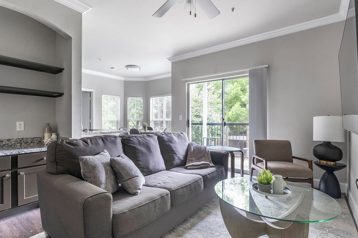 A modern living room with a grey sofa, a glass coffee table, and a TV mounted on the wall.