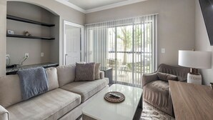 A living room with a sofa, armchair, coffee table, and a lamp. There is a sliding glass door leading to an outdoor area. - Landing Apartments Richmond (Richmond)