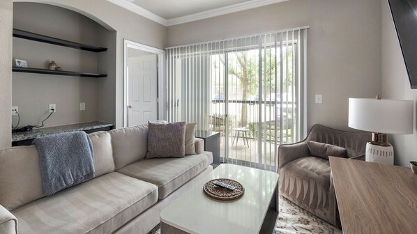 A living room with a sofa, armchair, coffee table, and a lamp. There is a sliding glass door leading to an outdoor area. - Landing Apartments Richmond (Richmond)