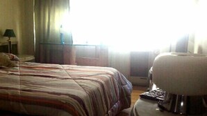 Quarto de hotel com cama, uma cadeira, abajur e janela com cortinas.