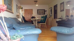 Uma sala de estar com um sofá azul, uma mesa de jantar com cadeiras e piso de madeira.