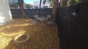 A patio area with a circular seating arrangement, a fire pit, and a fence.