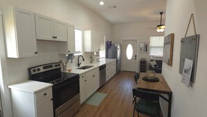 A kitchen with white cabinets, a black stove, a sink, and a dining area with a table and chairs.