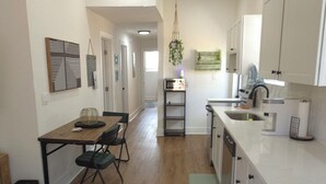 A modern kitchen with white cabinets, a wooden dining table, and a hanging plant.