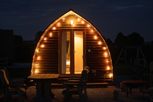 Une cabane en bois avec un toit en pente, des fenêtres éclairées et une porte.