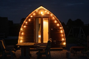 Une cabane en bois avec un toit en pente, des fenêtres éclairées et une porte.