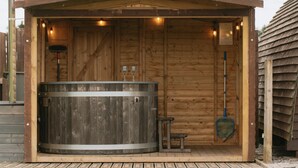 A wooden sauna structure with a large circular hot tub, a small bench, and a brush. - En-suite Wooden Cabin With Hot Tub (Langho)