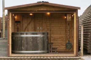 A wooden sauna structure with a large circular hot tub, a small bench, and a brush.