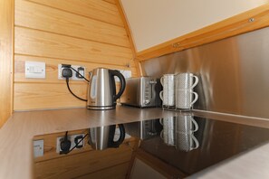 A kitchenette with a stainless steel toaster, a kettle, and two patterned mugs on a reflective countertop.