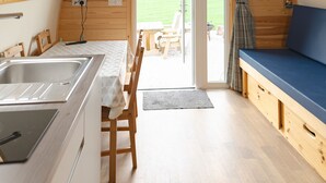 A cozy, wooden interior with a kitchen, dining area, and a large window overlooking a green landscape. - En-suite Wooden Cabin With Hot Tub (Langho)