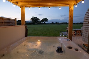 A hot tub with a wooden pergola overhead, surrounded by a grassy area and a wooden deck.