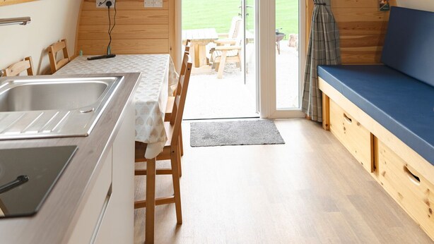 Un intérieur chaleureux, avec des éléments en bois, comprenant une cuisine, un coin repas et une grande fenêtre donnant sur un paysage verdoyant.