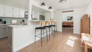 A modern kitchen with white cabinets, a central island with bar stools, a refrigerator, and a microwave.