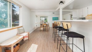 A modern kitchen with white cabinets, a wooden bench, and a dining area with chairs.