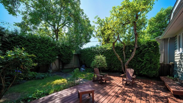 A wooden deck with a bench and chairs, surrounded by lush greenery and trees.