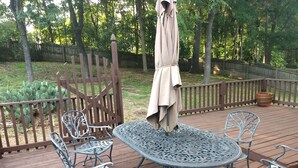 Une terrasse en bois, avec des tables et des chaises en métal, entourée d’une clôture en bois et d’arbres.