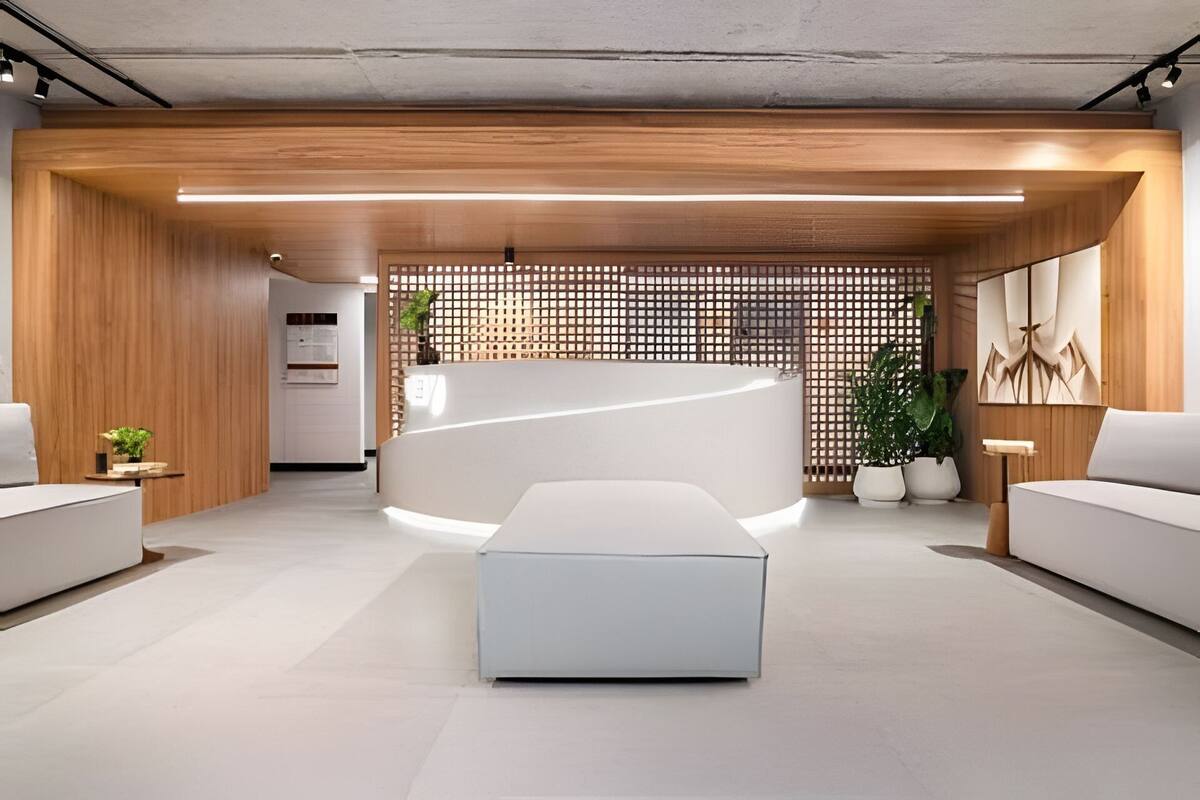 Un espace d’accueil moderne avec un comptoir central, des canapés blancs et une cloison en bois ornée d’un motif en treillis.
