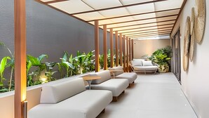 Un espace extérieur moderne, aménagé avec des canapés blancs et une table, entouré de plantes et d’une pergola en bois.