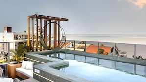 Une piscine à débordement située sur le toit, avec un hamac, offrant une vue sur la plage.