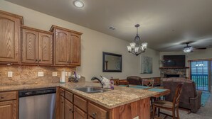 A kitchen with wooden cabinets, a dishwasher, granite countertops, a chandelier, and a dining area with a fireplace. - 2BR Village At Indian Point 503 near SDC-Free Tickets Daily up to $500 (Branson)