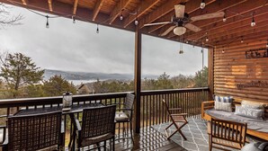 Una terraza cubierta al aire libre con muebles de mimbre, un ventilador de techo y vistas a un lago y montañas.