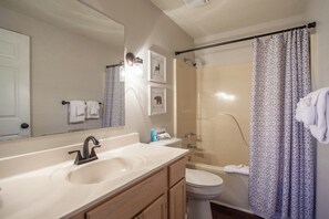 Features a large mirror, sink, toilet, and shower area with a patterned curtain.