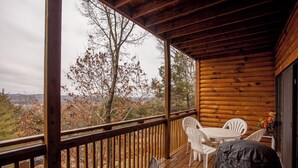 Een houten terras met een tafel en stoelen, met uitzicht op een landschap met bomen en een verre horizon.