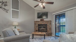 A living room with a stone fireplace, a ceiling fan, and a large window with blinds. - 2BR Village At Indian Point 711 near SDC-Free Tickets Daily up to $500 Value (Branson)