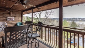 A wooden deck with a ceiling fan, a table with chairs, and a view of a river and hills.