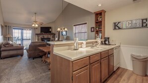 A spacious living area with a large island kitchen, wooden cabinets, and a stone fireplace.