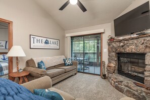 A living room with a stone fireplace, a sofa, a television, and a large window.