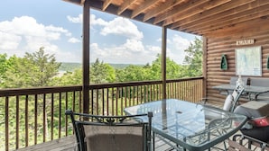 A wooden deck with a glass table and chairs, overlooking a lake and forest. - 2BR Village At Indian Point 905 near SDC-Free Tickets Daily up to $500 (Branson)