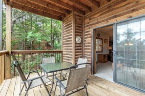 Une terrasse en bois avec une table et des chaises, une porte vitrée donnant sur l’intérieur et une vue sur la forêt environnante.