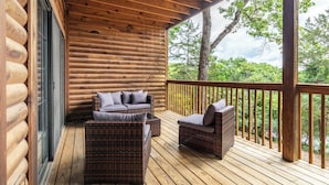A log cabin with a wooden deck, wicker furniture, and a view of trees.