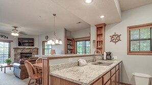 A spacious kitchen with granite countertops, wooden cabinets, a stone fireplace, and a dining area with a leather couch and wooden chairs.