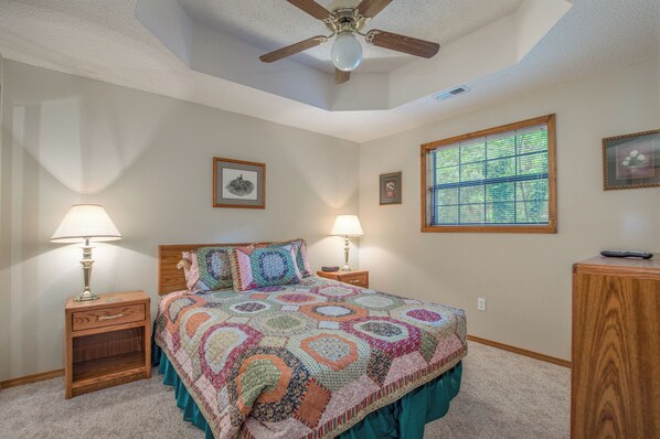 A bedroom with a large bed, two bedside tables with lamps, a ceiling fan, and a window with blinds.