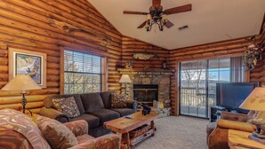A log cabin interior with a fireplace, a television, and a ceiling fan. - 2BR Village At Indian Point 1009 near SDC-Free Tickets Daily up to $500 (Branson)