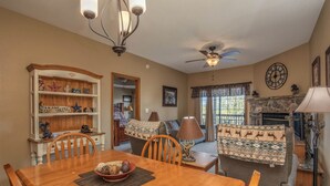 A dining area with a wooden table and chairs, a bookshelf, a sofa, and a fireplace. - 2BR Village At Indian Point 1106 near SDC - Free Tickets Daily up to $500 (Branson)