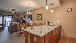 A spacious living area with a kitchen island, wooden cabinets, and a dining table. - 2BR Village At Indian Point 1106 near SDC - Free Tickets Daily up to $500 (Branson)