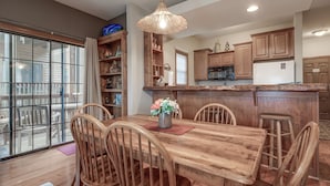 A dining area with a wooden table and chairs, a hanging light fixture, and wooden cabinets. - 2BR Village At Indian Point 1208 near SDC - Free Tickets Daily up to $500 (Branson)