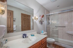Une salle de bain avec un lavabo blanc, un meuble-lavabo en bois, un grand miroir, une cabine de douche en verre et des toilettes.