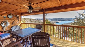 A wooden deck with a table and chairs, a ceiling fan, and a view of a lake and hills. - 2BR Village At Indian Point 1212 near SDC - Free Tickets Daily up to $500 (Branson)