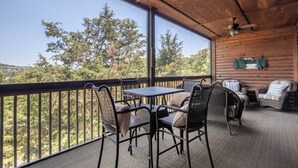 Un espace extérieur abrité, équipé d’une table et de chaises, d’un ventilateur de plafond et offrant une vue sur les arbres.