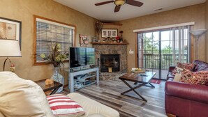 A living room with a stone fireplace, a television, a leather sofa, and a ceiling fan.