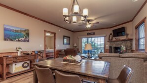 A spacious living room with a large wooden dining table, comfortable seating, a fireplace, and a scenic view through the windows. - 2BR Village At Indian Point 1504  near SDC - Free Tickets Daily up to $500 (Branson)