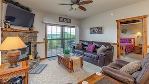 A living room with a fireplace, a television mounted above it, a leather sofa, and a ceiling fan. - 2BR Village At Indian Point 1307 near SDC - Free Tickets Daily up to 500 (Branson)