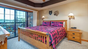 A bedroom with a large bed, a wooden nightstand, a ceiling fan, and a view through a sliding glass door. - 2BR Village At Indian Point 1307 near SDC - Free Tickets Daily up to 500 (Branson)