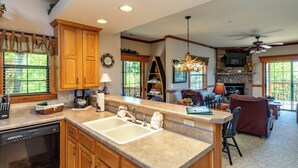 A spacious kitchen with wooden cabinets, a large island with a sink, and a dining area with a fireplace. - 2BR Village At Indian Point 2005 near SDC - Free Tickets Daily up to $500 (Branson)