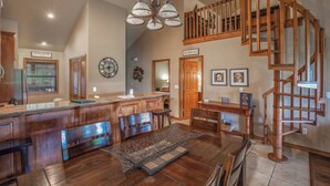 A spacious kitchen with wooden cabinets, a dining area with a large table, and a wooden staircase leading to an upper level. - 2BR+Loft Village At Indian Point 1910 near SDC- Free Tickets Daily up to $500 (Branson)