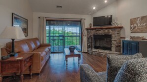 A living room with a sofa, a television, a fireplace, and a view of the outdoors. - 2BR+Loft Village At Indian Point 1910 near SDC- Free Tickets Daily up to $500 (Branson)